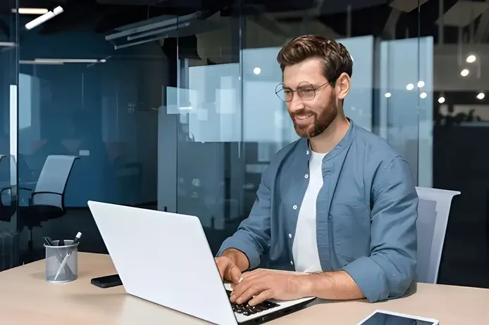 A man smiling while working at a laptop